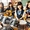 Four Japanese high school girls in a light music club, with a drum set, guitar, bass, and keyboard, sitting together in a classroom. They are smiling and having a good time.