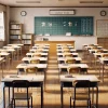 A classroom in a Japanese high school setting, with desks neatly arranged in rows according to a specific seating chart. The atmosphere is calm, with bright natural light streaming through the windows. The seating arrangement suggests a focus on specific students, with name tags visible on the desks. The classroom is clean, with traditional elements like a blackboard and wooden floors visible. There are no students present in the image, just the classroom setup.