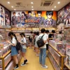 A bustling store with shelves displaying merchandise from a manga about high school students with superpowers. Customers browsing through manga, action figures, and posters. The atmosphere is energetic, and the store features colorful anime-themed decorations. Japanese customers are visible enjoying the displays.